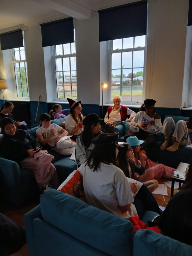 Group of children sitting on blue sofas in a bright room, working on papers and crafts around a low table.