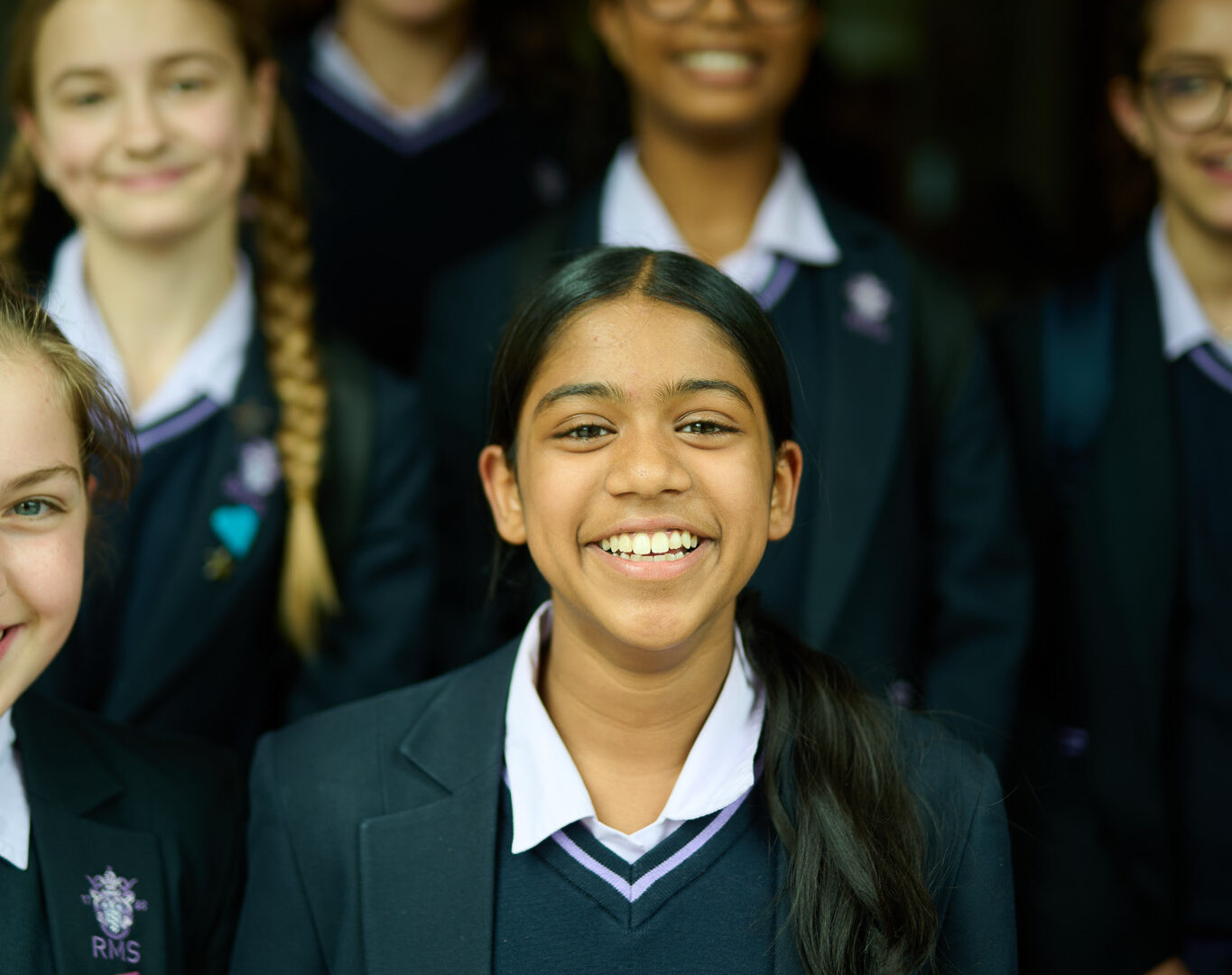 Smiling girl in a navy school uniform in the foreground with other students in the background.