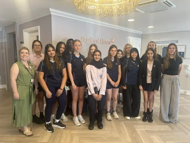 Group of students and two adults posing in a Burford House lobby, some in navy uniforms and others in casual clothes, smiling at the camera.