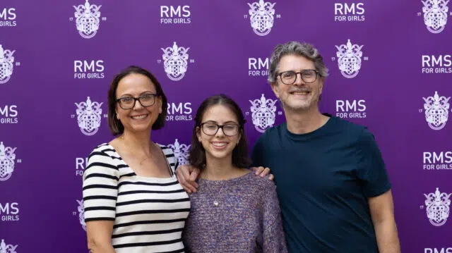 Three people smile for a photo in front of a purple RMS for Girls backdrop.**Note: keep as concise alt text**